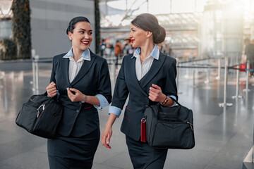 Smiling pretty flight attendants with bags talking in the terminal