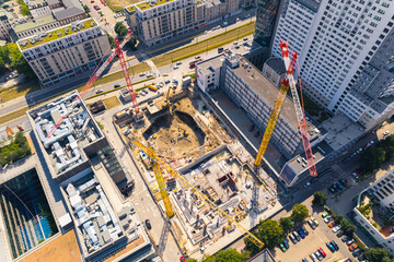 Construction workers building housing units or new skyscrapers between two buildings. Three cranes seen from aerial drone perspective. High quality photo
