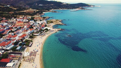 Sarti in Greece. Laid-back village with beachfront promenade around a rocky bay. Turquoise shallow water. Tourists relaxing. Aerial view. High quality photo