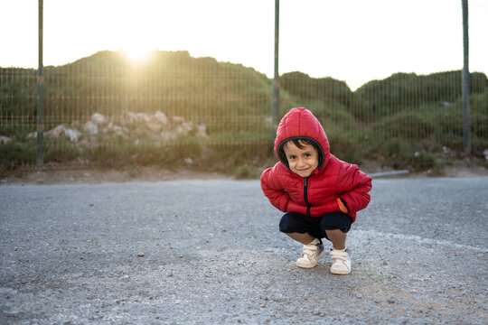 2 - 3 year old boy with jacket and hood in a suburb at sunset