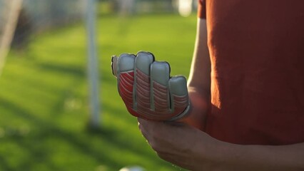Young man football goalkeeper wearing gloves while standing at the soccer stadium. Slow motion.
