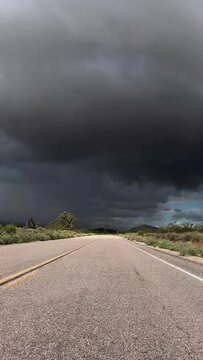 Driving towards dark desert storm clouds in Mojave National Preserve in Southern California. Vertical video.