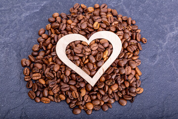 Coffee beans with a wooden heart on a dark background.