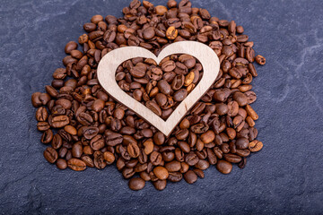 Coffee beans with a wooden heart on a dark background.