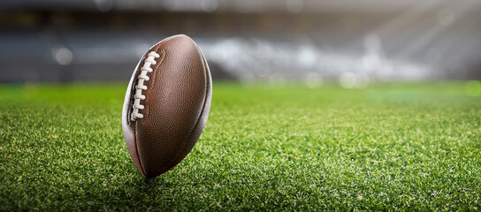 American football ball on the grass of a stadium - copyspace - obrazy, fototapety, plakaty