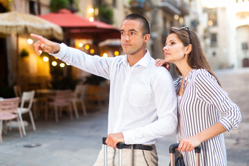 Fototapeta premium Young positive tourist couple walking around foreign city on summer day, pointing at sights