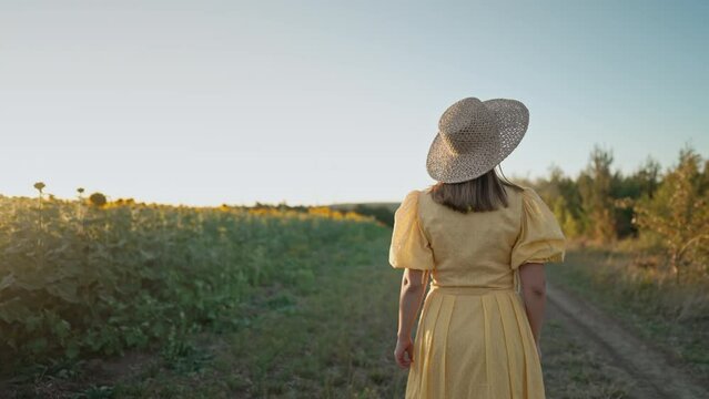 Attractive woman in old-fashioned dress walking alone near sunflowers field. Vintage fashion, amazing adventure, countryside, rural scene, natural lifestyle.