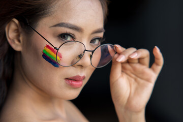 Portrait of female face wear glasses with colorful painted rainbow on cheek and looking at camera. LGBT flag. Equality and support of diversities to people.