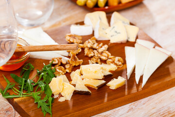 Delicious cheese assorted with honey and walnuts on a wooden board, decorated with fresh arugula on top