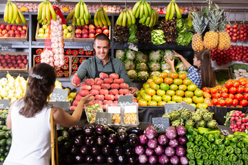Friendly shop assistans selling fresh fruits and vegetables to woman