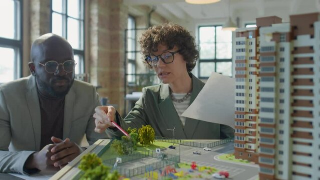 Caucasian female architect presenting real estate development model to African American male client in office