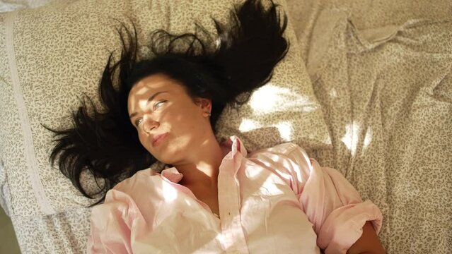 Caucasian girl wakes up and stretches in bed since morning. A woman opens her eyes when the sun hits her from the window. High quality 4k footage
