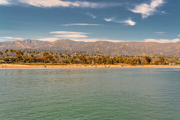 Santa Barbara beach with beautiful palm trees, Pacific Ocean, mountains, and cloudy sky on background - obrazy, fototapety, plakaty