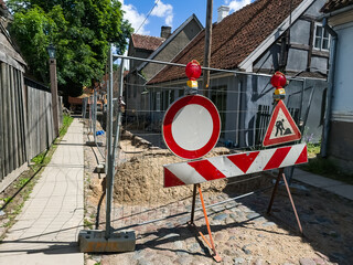 Street repair in summer day. Sand, road signs, fence and houses.