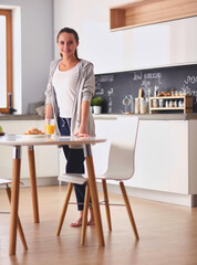 Young woman with orange juice and tablet in kitchen.