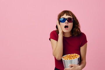 Confused concentrated cute redhead lady in red t-shirt 3D glasses eat popcorn watch movie posing isolated on over pink studio background. Copy space Banner. Fashion Cinema concept. Entertainment offer