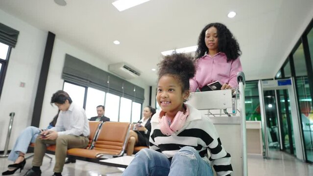 4K African woman with her kid walking to airline ground staff at check in counter and get boarding pass ticket in airport terminal. Airline service business and airplane transportation concept