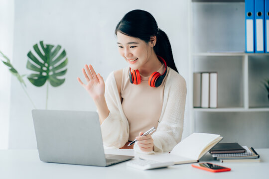 Young adult happy smiling Hispanic Asian student wearing headphones talking on online chat meeting using laptop in university campus or at virtual office. College female student learning remotely