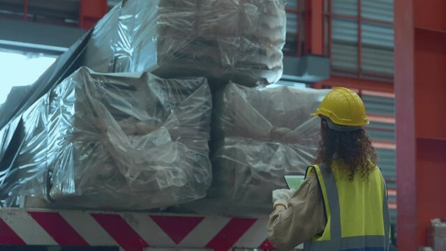 Industrial woman curly hair engineer wear safety uniform with hardhat checking metal sheet on cargo truck before shipment to customer in warehouse store factory workshop, logistics and transportation