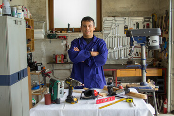 Image of a smiling blacksmith in his workshop with a bench with the tools of the trade in front....