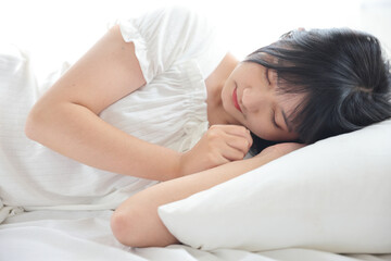 Fototapeta na wymiar Beautiful young Asian woman sleeping on bed relaxing in the morning light with white room