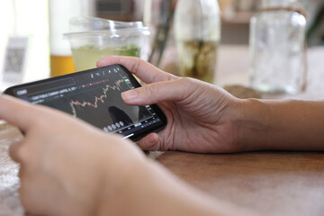 Fototapeta na wymiar Woman hand using a smartphone for Stock exchange trading online in the coffee shop, business concept