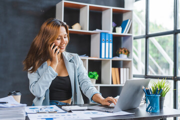 Young pretty asian accountant calling mobile phone with client to analyze sales growth in the global workplace market.