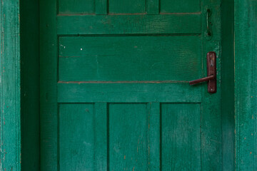 Fragment of an old green wooden door of a village house. Cracked paint on boards. Two door handles.