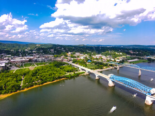 Fototapeta na wymiar aerial shots of the flowing waters of the Tennessee River with the Walnut Street Bridge and the Chief John Ross Bridge over the water surrounded by lush green trees and plants with blue sky and clouds