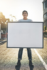 Young man holding an empty sign, board or placard while standing outside in the city street. Portrait of one happy, smiling and cheerful guy making an annoucement, showing an ad or doing promotion