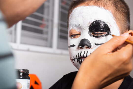 Portrait of woman applying color brush to child face for party at home, family Asian mother and kid son getting makeup halloween face painting look like ghost, Happy halloween day concept