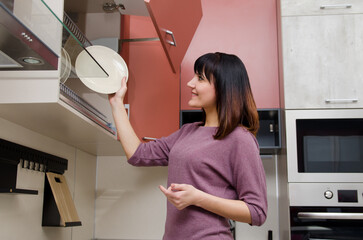 A young smiling woman puts a plate in a dish rack in the kitchen.