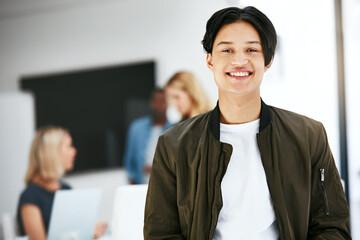 Happy, confident and carefree business man relaxing in a modern office with colleagues in the background. Portrait of a young proud professional smiling, taking a break to rest at work