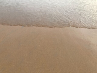 smooth and clear brown sand beach with white sea waves in bright natural daylight