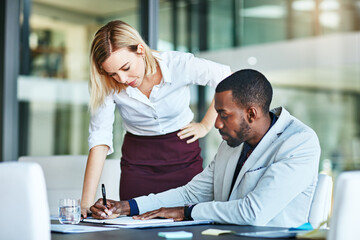 Business people working together in a modern office, writing and reading paperwork. Director training an assistant and helping him with his report. Woman coaching a new employee at work