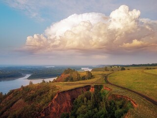 In large clouds, the light of the setting sun and the warm evening light flood the trees on the hill, the clay mountain and the reflection of the clouds in the water. river Ob.
