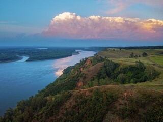 a high bank of clay with fields and trees, clouds in the sunset light, the sun and the riverbed of the Ob