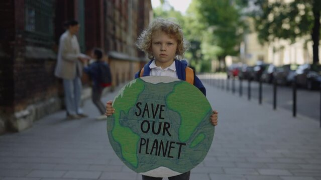 Little boy standing outdoor against enviroment pollution loooking at camera. Little eco activist demostration on the street. Eco concept