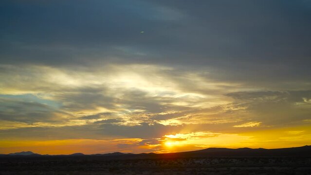 Golden sunrise above the mountain horizon in silhouette - cloudscape time lapse