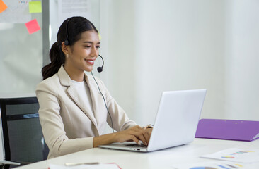 Young asian businesswoman in brown suit and headset with mic typing on laptop computer keyboard while meeting online through internet connection. Working concept social distancing.