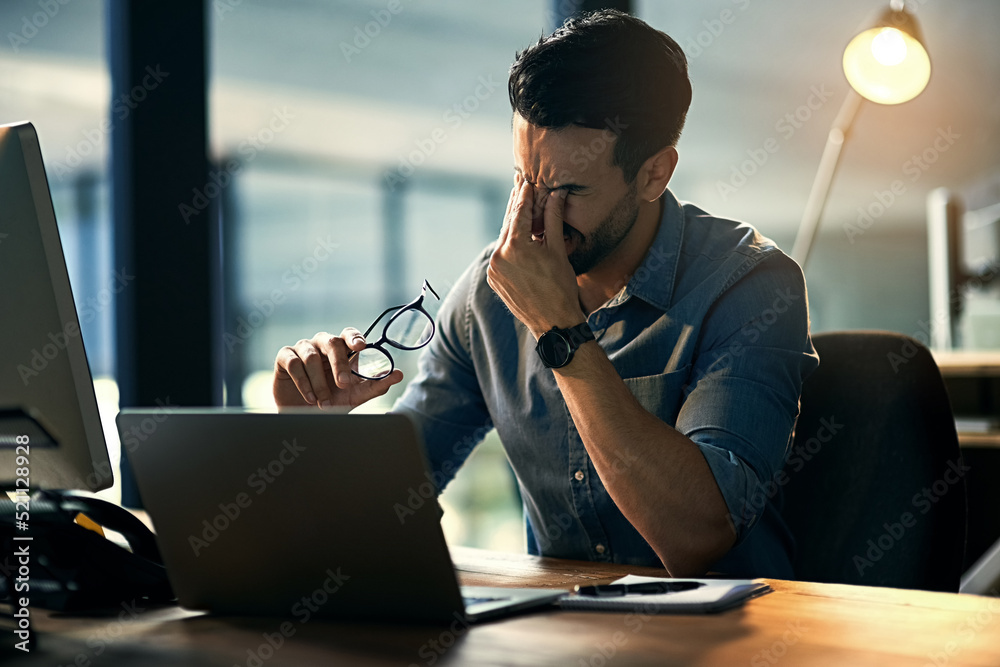 Poster Struggling with occupational stress. Shot of a young businessman experiencing stress during a late night at work.