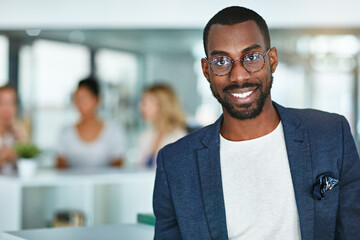 Intelligent smiling face of a businessman, professional or corporate worker in a busy office. A happy and smart portrait of a friendly black business man with workplace as background and copy space