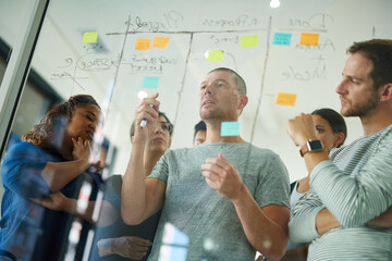Business people brainstorming, planning and thinking of ideas on a glass board. A group or team of...