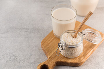  A jar of raw rice and rice milk in a glass on a plank on a gray background. Healthy food concept, alternative milk.