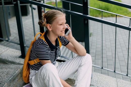 A beautiful girl is sitting on the stairs at school in between classes and talking on the phone - Powered by Adobe
