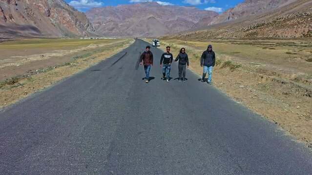 Group Of Friends Walking On Asphalt Road In Sarchu, Himachal Pradesh, India. drone pullback ascend