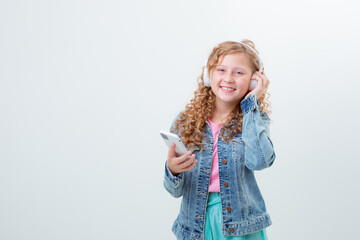 a teenage girl with a backpack in headphones holds a phone on a white background