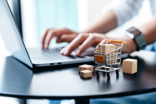 Parcel box in trolley on table with hand of young woman using laptop for shopping, Buy products from entrepreneurs via the Internet, E-commerce,  Online Shopping Concept.