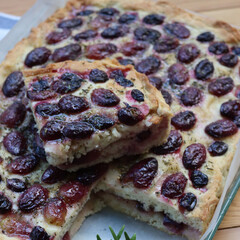 Sliced Italian Focaccia bread with sweet black grape and rosemary on a wooden table. Traditional dessert from Tuscany in Italy called “schiacciata con l'uva”