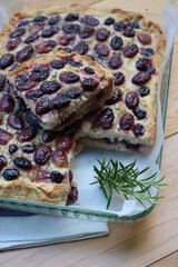 Sliced Italian Focaccia bread with sweet black grape and rosemary on a wooden table. Traditional dessert from Tuscany in Italy called “schiacciata con l'uva”